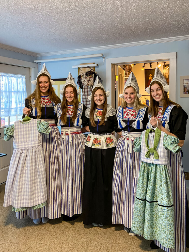 Young ladies dressed in Dutch costumes stand together showing off their costumes. 

