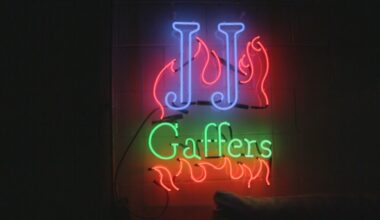 A bright neon sign reads ‘J.J Gaffers’ against a dark studio wall.