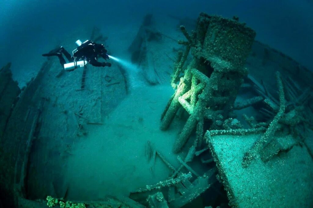 Diver pointing a flashlight at a shipwreck.