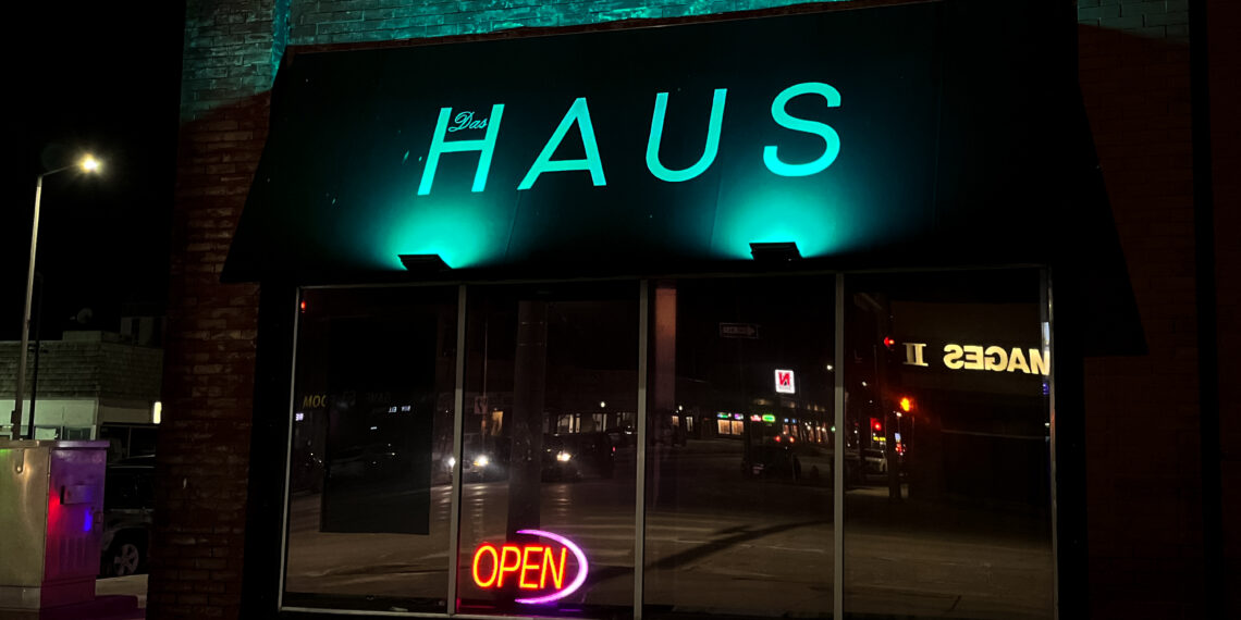 Das Haus bar from the outside, with an open sign in the window and a teal glow shining on the Das Haus logo.