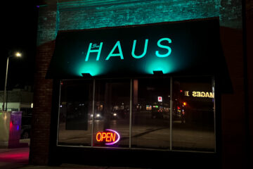 Das Haus bar from the outside, with an open sign in the window and a teal glow shining on the Das Haus logo.