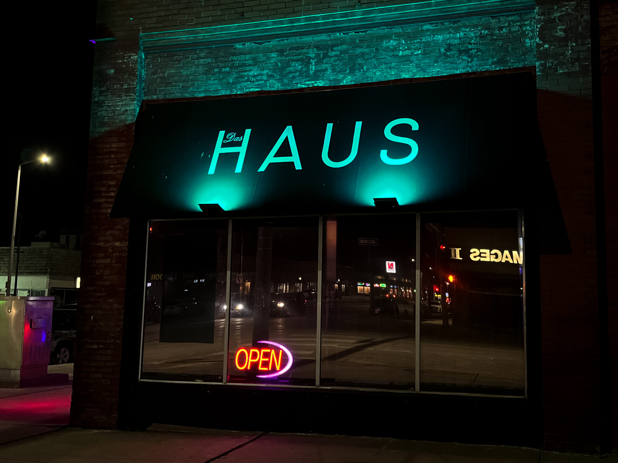 Das Haus bar from the outside, with an open sign in the window and a teal glow shining on the Das Haus logo.