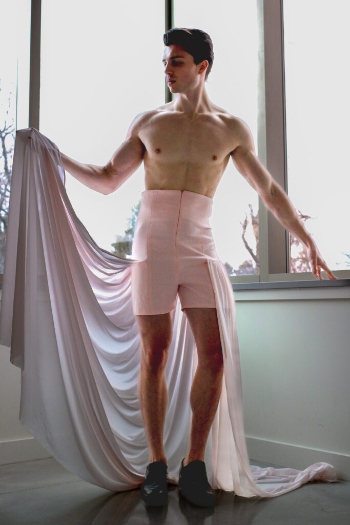 A model holds up the flowing train attached to his light pink shorts. 
