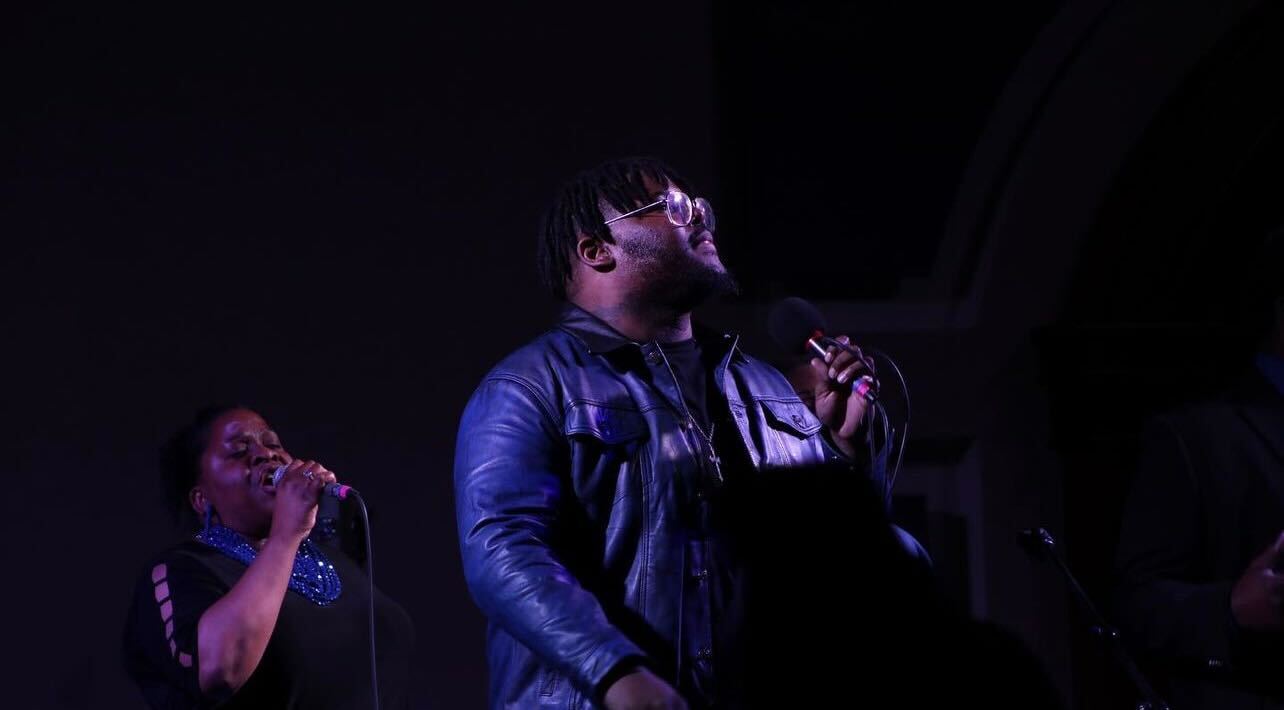 Man singing on stage with female vocalist in background.