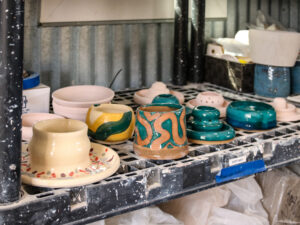 Glazed pottery pieces sit on a shelf surrounded by other unfinished clay pieces.