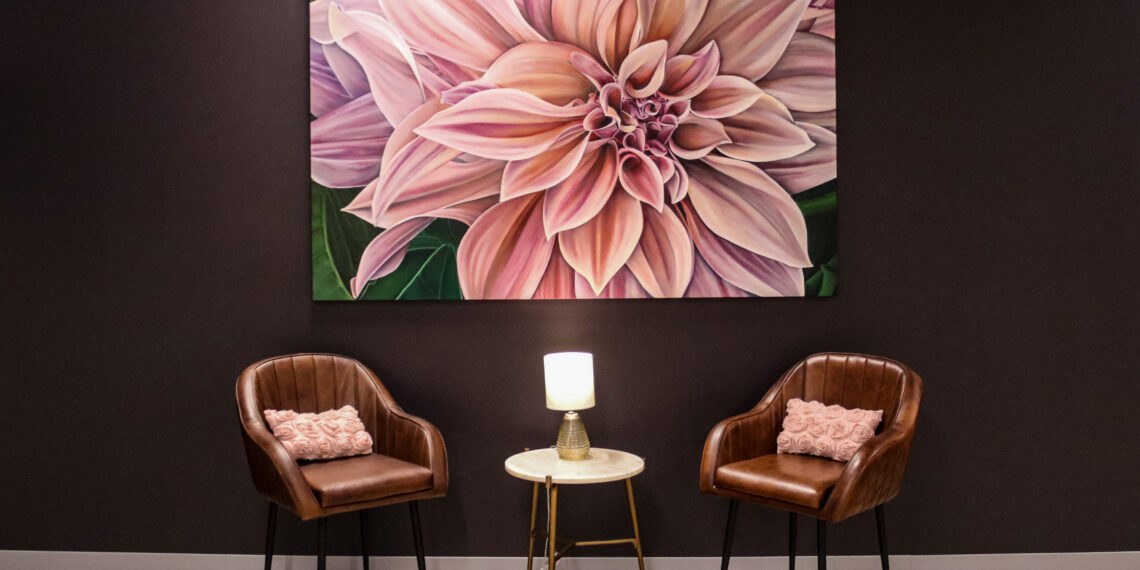 A large, pink flower hangs on a black wall of artist Jess Quinn’s studio above two brown chairs on both sides of a small circle table.