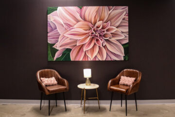 A large, pink flower hangs on a black wall of artist Jess Quinn’s studio above two brown chairs on both sides of a small circle table.
