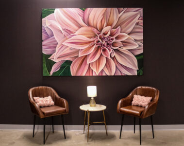 A large, pink flower hangs on a black wall of artist Jess Quinn’s studio above two brown chairs on both sides of a small circle table.