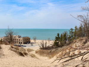 An image on top of a sand dune, overlooking the Indiana Dunes National Park Pavilion on the beach with Lake Michigan in the background.