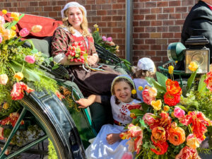 Young ladies dressed in Dutch costumes sit on a carriage covered in flowers.