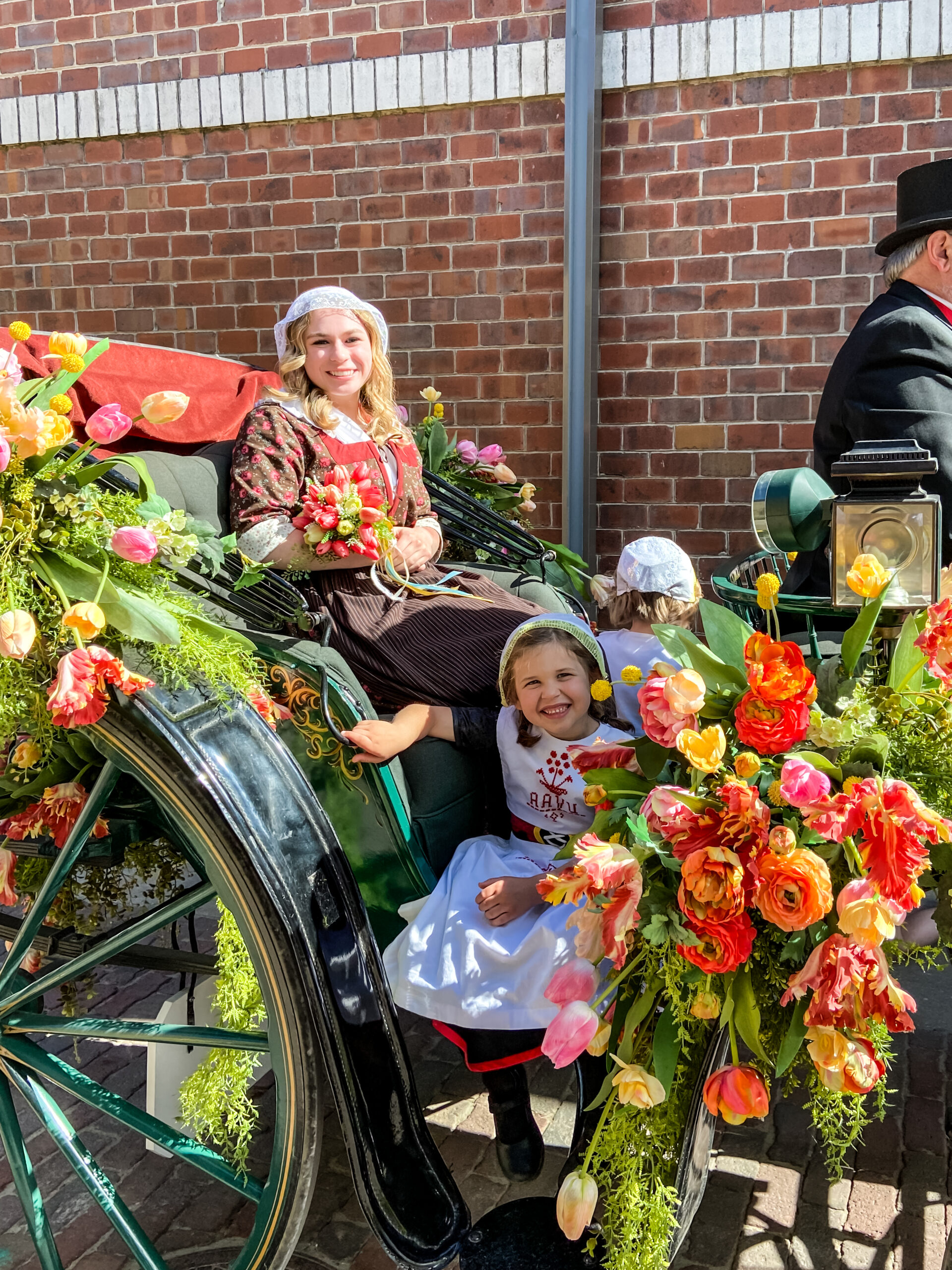 Young ladies dressed in Dutch costumes sit on a carriage covered in flowers.