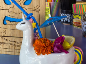 A clear drink served in a unicorn-themed cup garnished with a lemon slice and colorful flowers.
