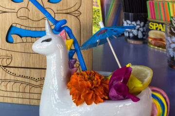 A clear drink served in a unicorn-themed cup garnished with a lemon slice and colorful flowers.