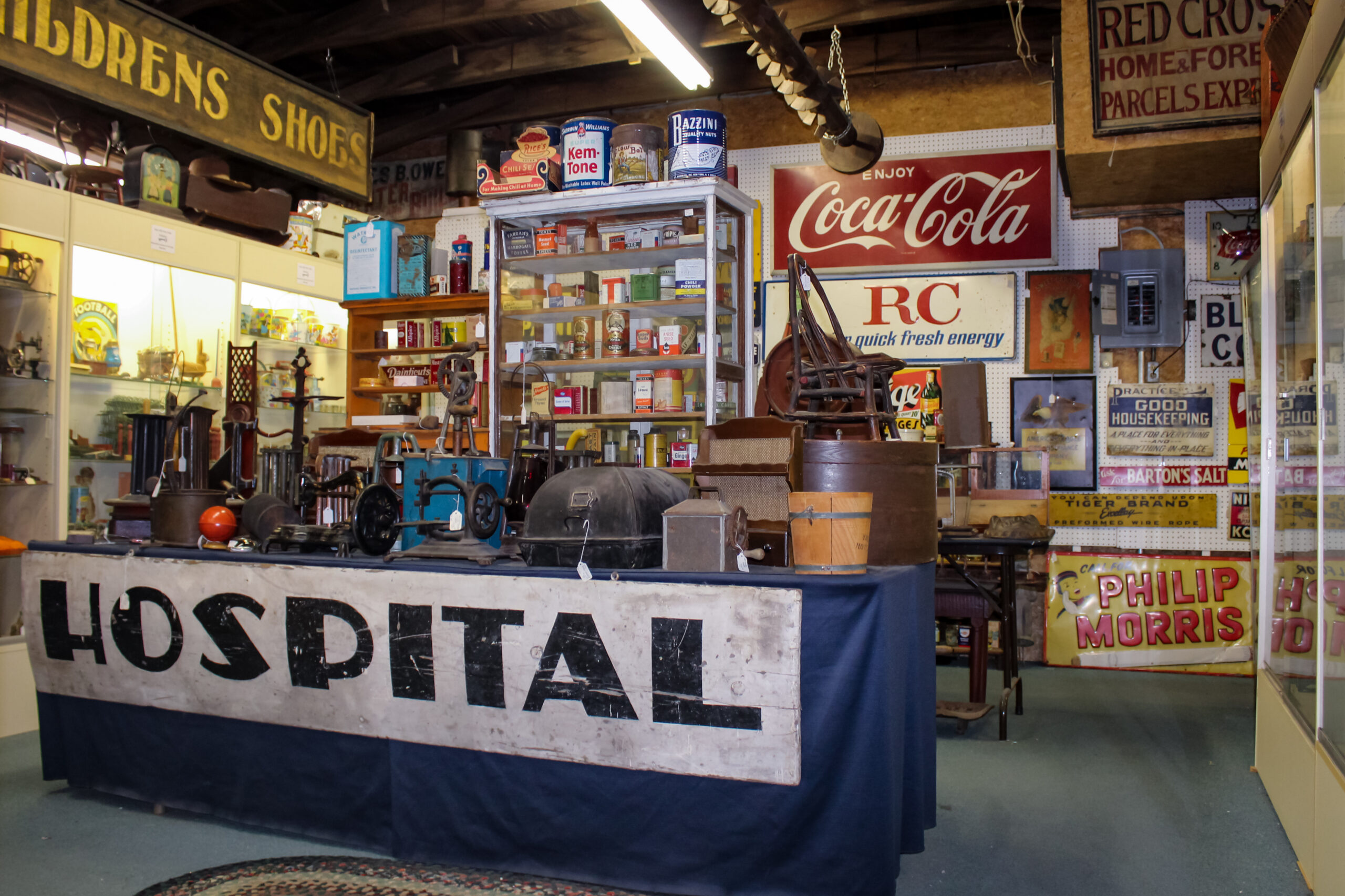 An image with various signs hanging on a wall, cabinets filled with antiques and a blue display table with a sign that says “Hospital” on the front.