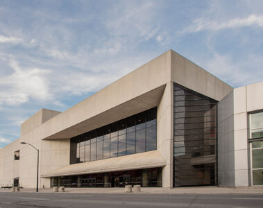A photo outside the Des Moines Civic Center. The building is large with harsh cement angles and rows of large windows.
