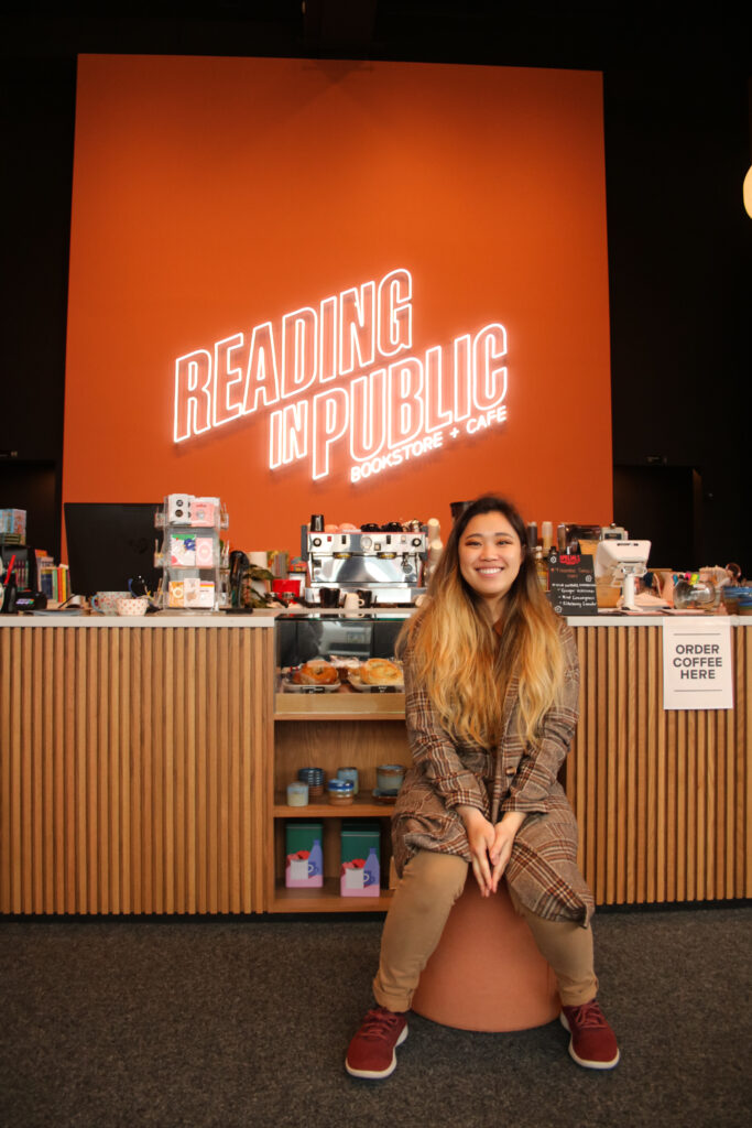 Linzi Murray, owner, poses before the Reading in Public sign on the back wall of the bookstore.
