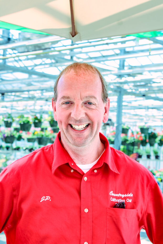 A headshot of the owner of Countryside standing inside the store and wearing one of their bright red uniform shirts. 

