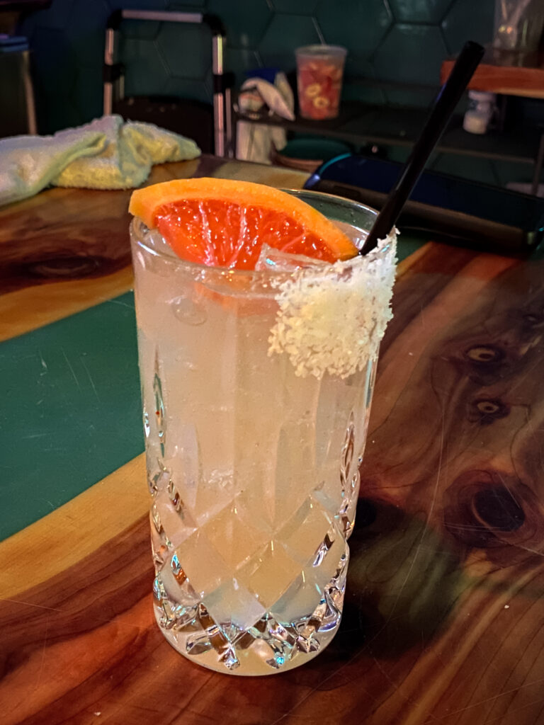  A light orange drink served in a tall glass garnished with a grapefruit wedge. 
