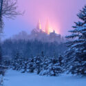 Snowy woods below with a catholic church sitting on the hill above.