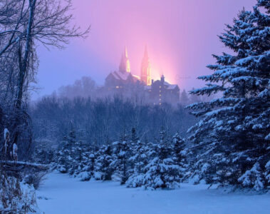 Snowy woods below with a catholic church sitting on the hill above.