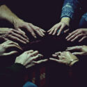 A photo shows several hands on a table in a circle.