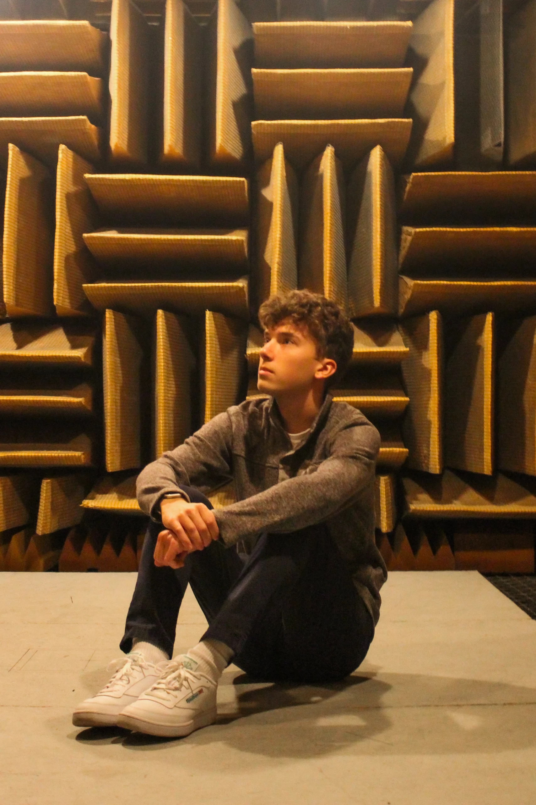 Nate Eisenmann, the author of the article, is sitting on the ground. Behind him, there is a wall lined in soundproofing tiles.