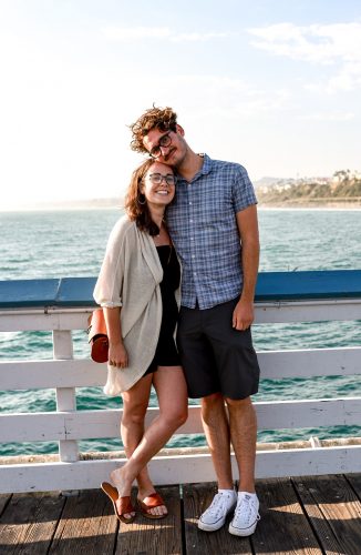 Couple Annaliese Franklin and Jared Kassebaum standing together at a beach pier in Southern California.